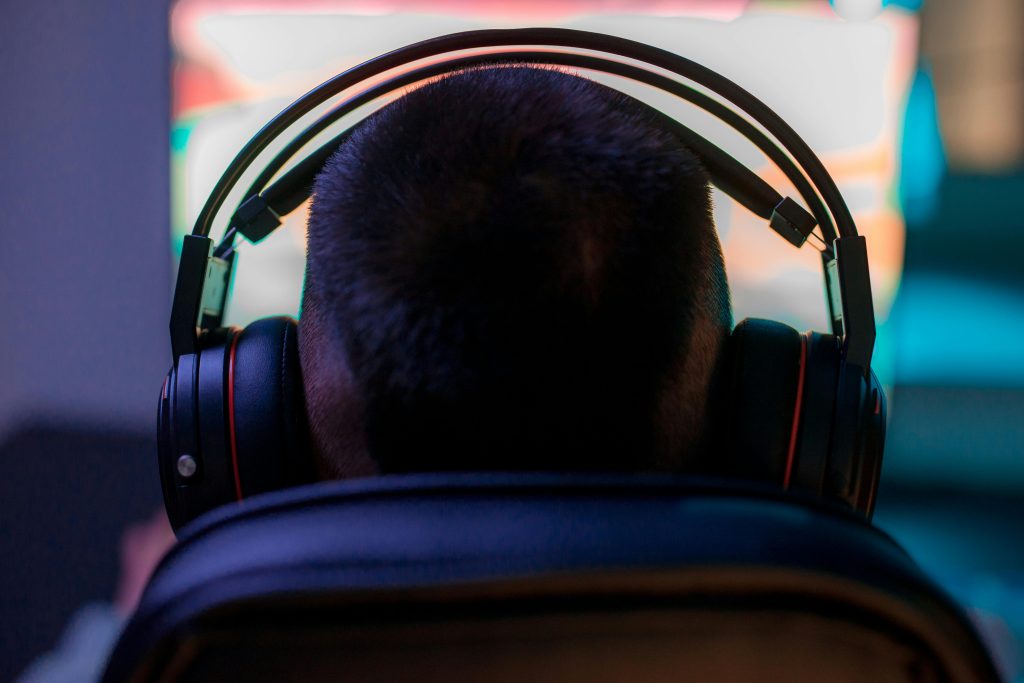 A man wearing headphones intently playing a video game on a computer in a dark room.